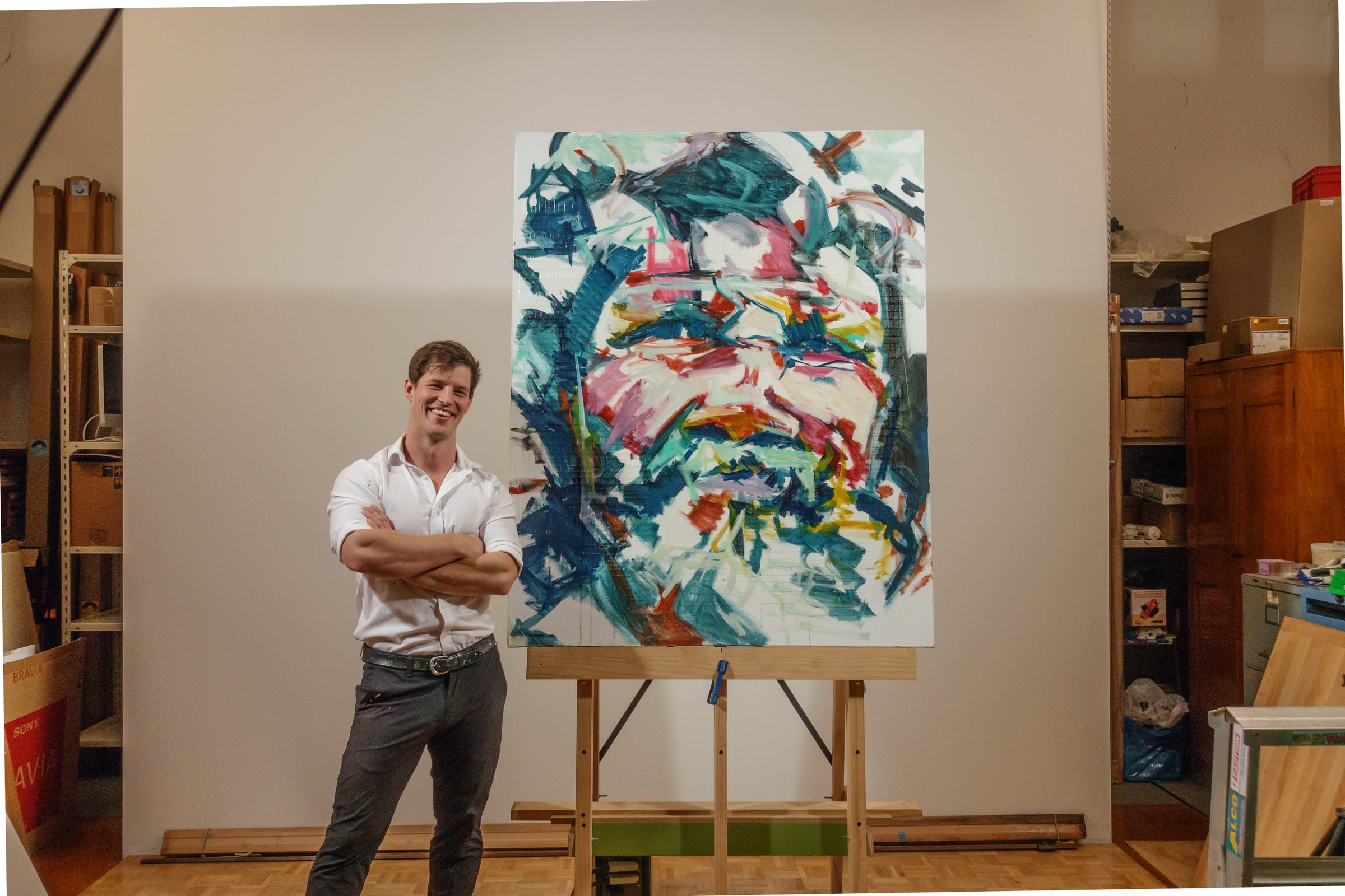 Seb Gower in his studio beside a large, wildly colourful portrait painting